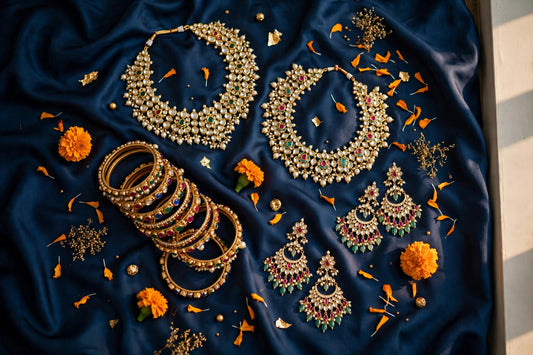 Kundan necklace sets, bangles and chandbali earrings arranged on navy silk with marigold flowers